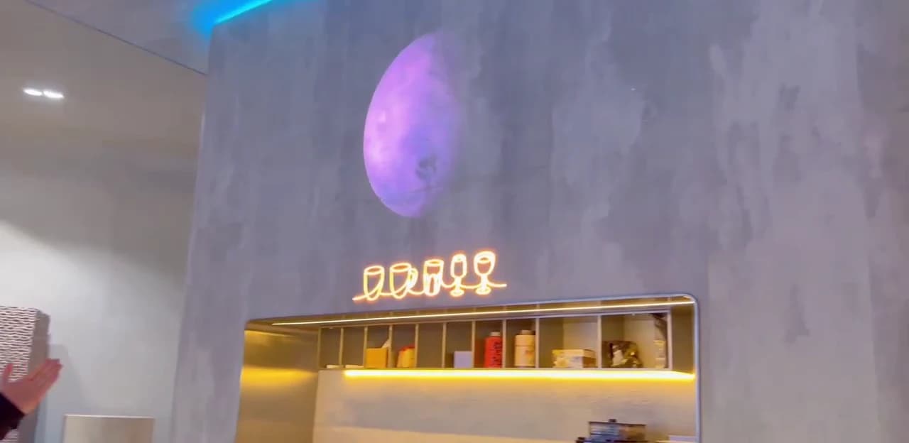 An Econiclay-clad wall in the PHOMI showroom showing a large planet image and illuminated drink icons above a lit counter recess.