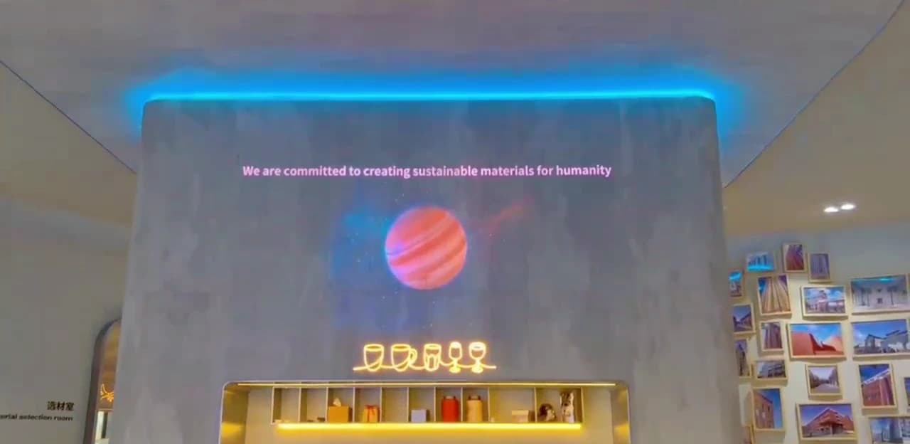 A PHOMI showroom wall finished in Econiclay, displaying a line of text and a glowing planet image across the surface, lit by a blue cove light above and illuminated glassware graphics below.